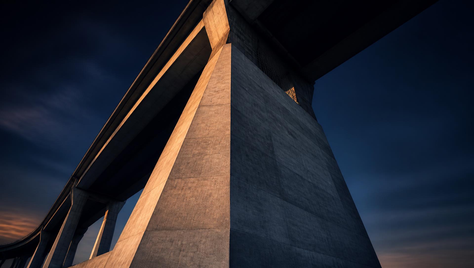 Pilar e vãos de concreto de uma ponte vistos de baixo ao anoitecer, representando crédito como estrutura e não urgência